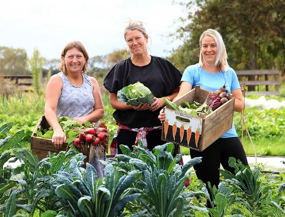 Three people standing in the Hamlin Road Farm garden holding produce